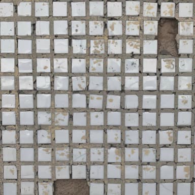 Close view of worn mosaic tile with missing pieces and cracked grout